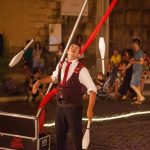 Giocoliere in Piazza Cavour a Tarquinia durante il Divino Etrusco, spettacolo di strada tra pubblico e luci serali.