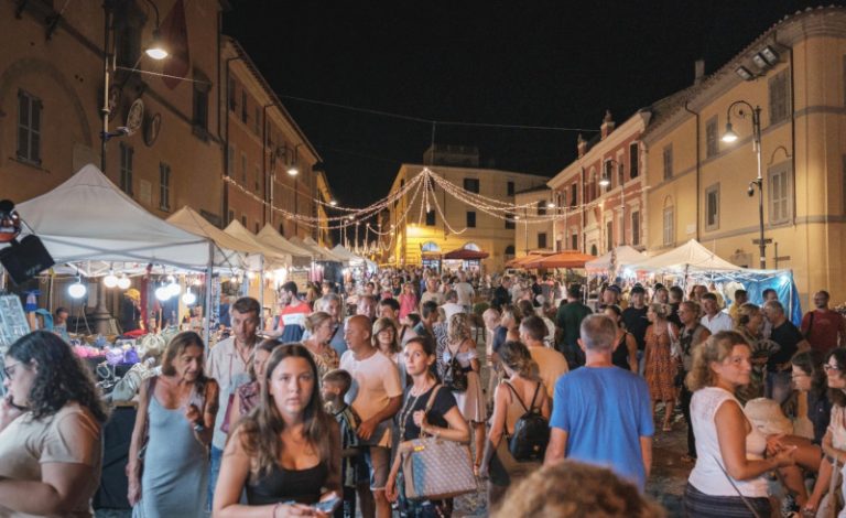 Vista notturna del centro storico di Tarquinia durante il DiVino Etrusco, con stand illuminati, folla e atmosfera festosa.