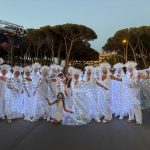 Donne in abiti bianchi illuminati da luci led durante il Carnevale estivo 2025 a Tarquinia Lido