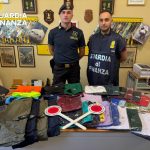 Guardia di Finanza Tarquinia espone abbigliamento e accessori contraffatti sequestrati durante i controlli estivi.