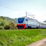 Treno espresso italiano in corsa ripreso lateralmente su linea ferroviaria panoramica.