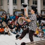 Artista di strada in equilibrio con cappelli durante uno spettacolo del Circo Verde davanti al pubblico.