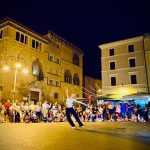 Chiara Perticarari di Arteritmica si esibisce in piazza Cavour a Tarquinia durante la prima serata del Divino Etrusco 2025 davanti a un folto pubblico.