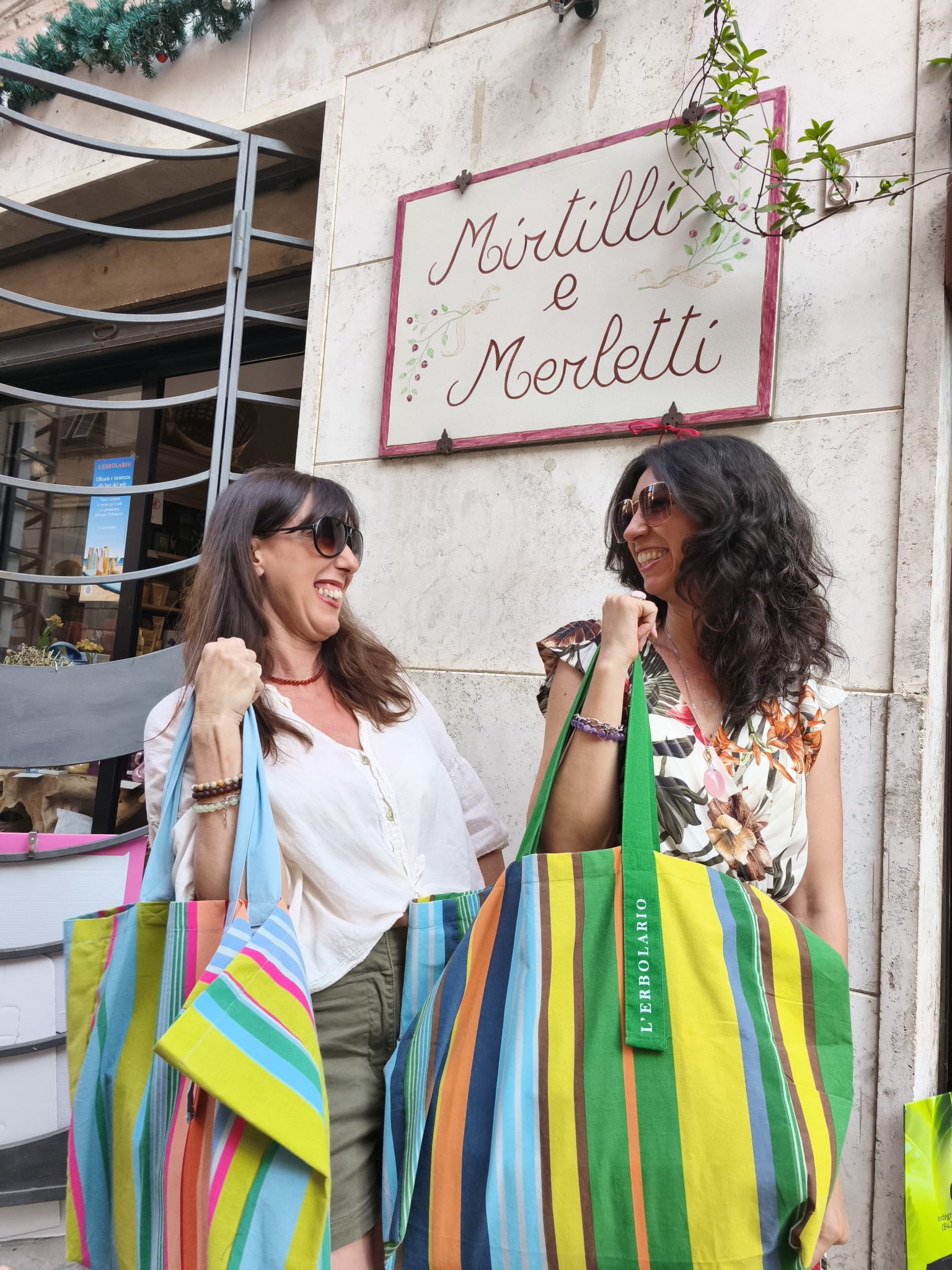 Alessandra e Roberta, cuore di Mirtilli e Merletti a Tarquinia, sorridono con le borse L’Erbolario: benessere, oggettistica e idee regalo originali.