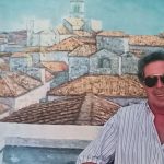 Il pittore tarquiniese Giuseppe Cappellacci davanti a un’opera con i tetti di Tarquinia, in occasione della mostra “Solitudini d’agosto” 2025