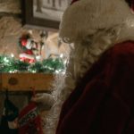 Babbo Natale di spalle di fronte a un camino decorato
